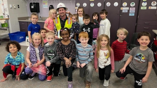 An image of a group of children posing with a Triangle worker in a hard hat and safety vest