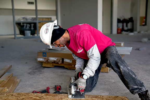An image of a male worker with hardhat sawing piece of wood