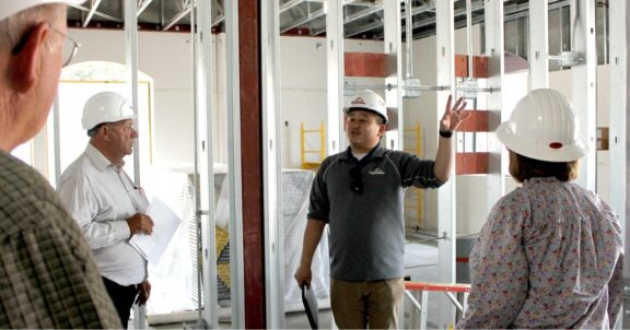 An image of a male engineer with hardhat leading a meeting with 3 other workers all wearing hardhats